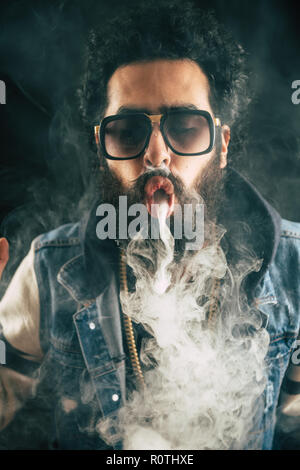 Young man with beard throwing a cloud of steam. Black background. Vaping an electronic cigarette with a lot of smoke Stock Photo