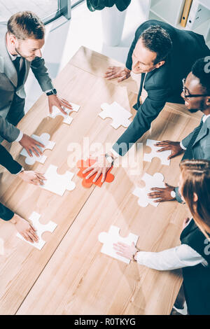 high angle view of multiracial businesspeople assembling puzzle on conference table Stock Photo