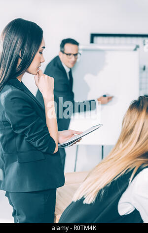 thoughtful asian businesswoman looking at notebook while her partner making presentation Stock Photo