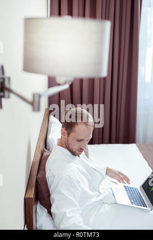 Blonde-haired businessman chilling on bed in luxurious hotel room Stock Photo