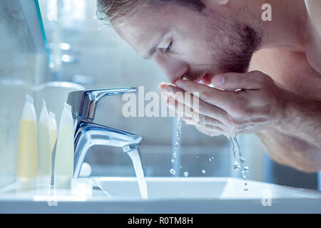 Bearded handsome man washing his face in the morning in light bathroom