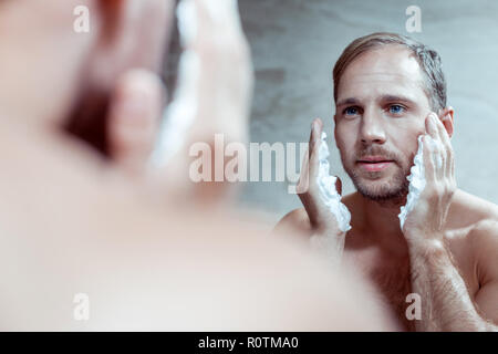 Handsome blue-eyed man using shaving foam while shaving face Stock Photo