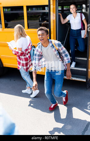 laughing african american schoolboy running out of school bus with female classmates Stock Photo