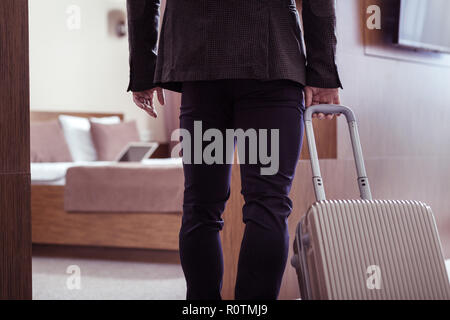 Businessman wearing dark jacket taking his luggage into hotel room Stock Photo