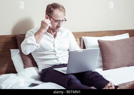 Businessman wearing dark trousers and white shirt lying on hotel bed Stock Photo