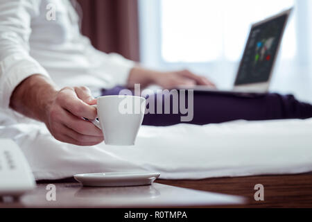 Businessman wearing suit lying on bed while drinking some tea Stock Photo