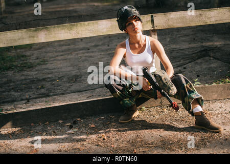 young female paintballer in white singlet and goggle mask holding paintball gun outdoors Stock Photo