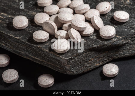 Pile of pills or medication on a slab of black rock. Stock Photo