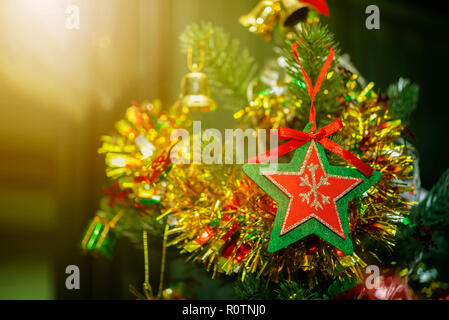 Merry Christmas background concept. Closeup of red star with green frame hanging on Christmas tree with blurred golden light from window. Holiday part Stock Photo