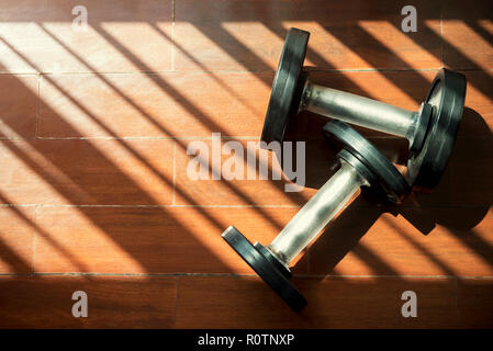 Fitness and healthy concept. Dumbbells on floor with shadow and light fron window in gym. Stock Photo
