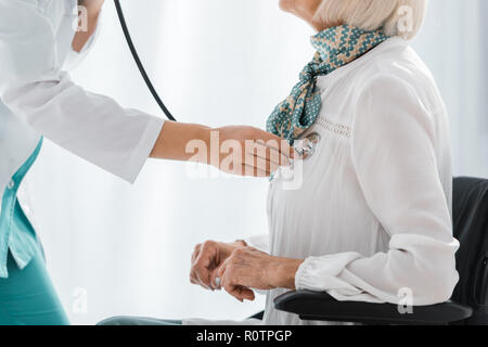 close up of young female doctor examining with stethoscope disabled senior woman Stock Photo