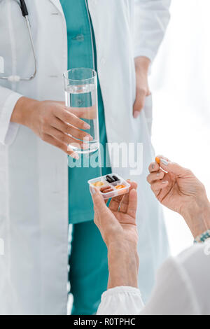 close up of young female doctor giving pills and glass of water to senior woman Stock Photo