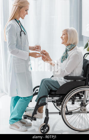 young female doctor giving pills to disabled senior woman Stock Photo