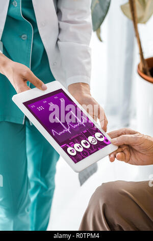 close up on doctor and patient hands holding digital tablet with cardiogram on screen Stock Photo