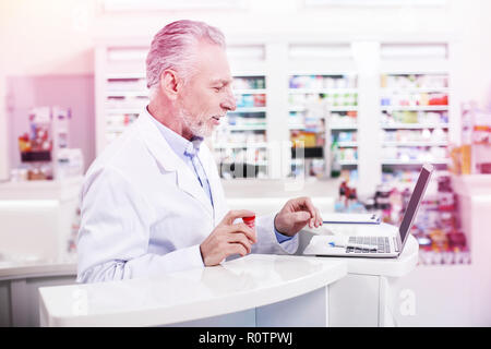 Elder grey-haired pharmacist working with a laptop Stock Photo