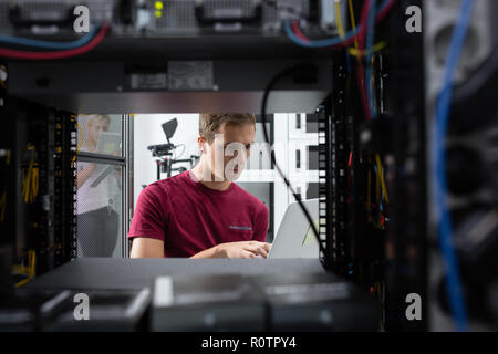 Male Server Engineer Works on a Laptop in Large Data Center. Stock Photo