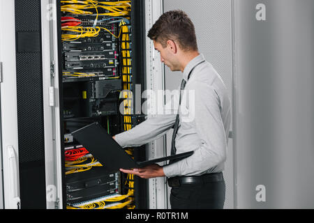 young man connecting wires in server cabinet while working with supercomputer in data center Stock Photo