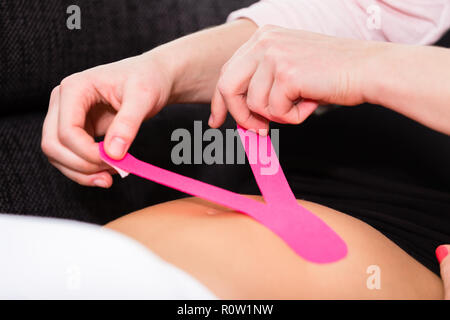 Therapist applying kinesio tape on woman's stomach Stock Photo