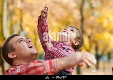 Father and son are playing and having fun in autumn city park. They posing, smiling, playing. Bright yellow trees. Stock Photo