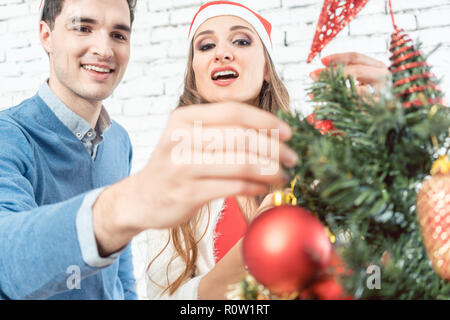 Man putting Christmas ornament on tree Stock Photo