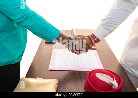 An African business man and woman shake hand over a typed document, over a corporate table in an office with white background. Stock Photo