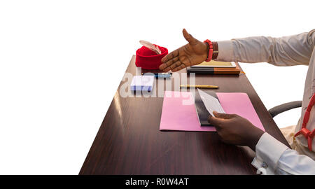 An African business man extends hand to shake after signing a cheque at a table showing his redcap with feather, beaded necklace, jotter, pink file, w Stock Photo