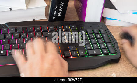 Hand typing on a colored keyboard. Motion blur. Working human hands detail. Computer mouse. Books close-up. Office wood table. A lettering secure www. Stock Photo