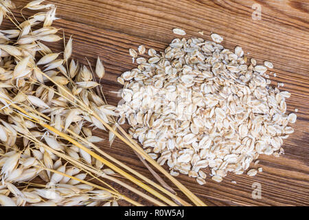 Rolled oats and common oat spikes on brown wood. Avena sativa. Oat flakes pile close-up. Decorative dry ears, cereal grains, vintage wooden backgroud. Stock Photo