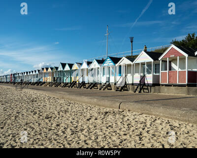 A row of brightly coloured beach huts along the seafront at Southwold against a bright blue sky Stock Photo