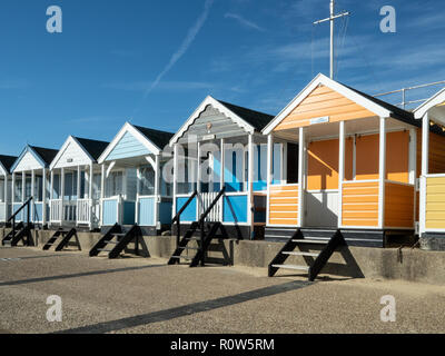 A row of brightly coloured beach huts along the seafront at Southwold against a bright blue sky Stock Photo