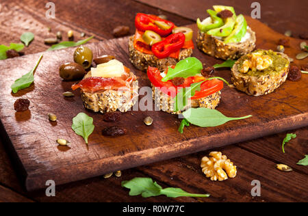 Closeup of different mini sandwiches on a cutting board and wooden table. Stock Photo