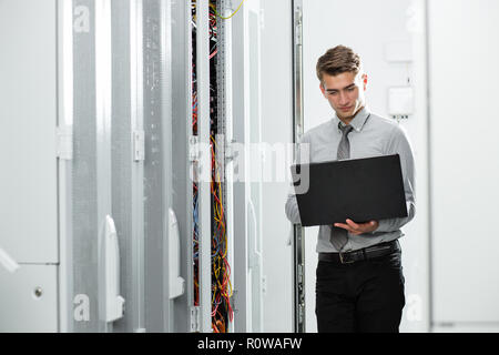 Male Server Engineer Works on a Laptop in Large Data Center. Stock Photo