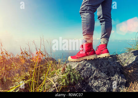 Close up of red shoes of traveller standing on mountain peak with blue sky at sunset. Freedom lifestyle. Good life and healthy concept. Picture for ad Stock Photo