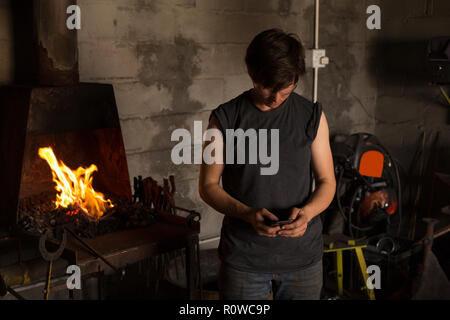Female metalsmith using mobile phone in factory Stock Photo
