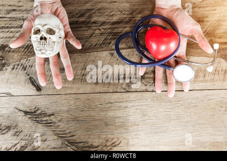 Stethoscope and red heart on left hand, skull on right hand. Choosing healthcare and die concept with free copy space for text. Stock Photo
