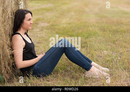 Woman relaxing against hay bale in the field Stock Photo