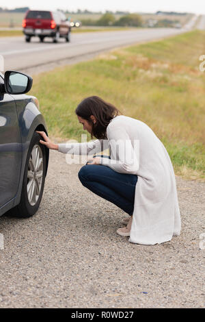 Woman checking car tyre during breakdown Stock Photo