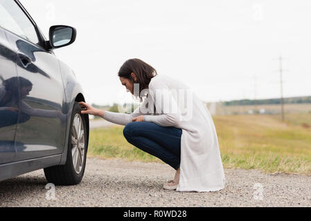 Woman checking car tyre during breakdown Stock Photo
