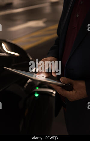 Businessman using digital tablet while charging electric car Stock Photo