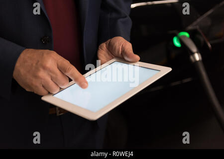 Businessman using digital tablet while charging electric car Stock Photo