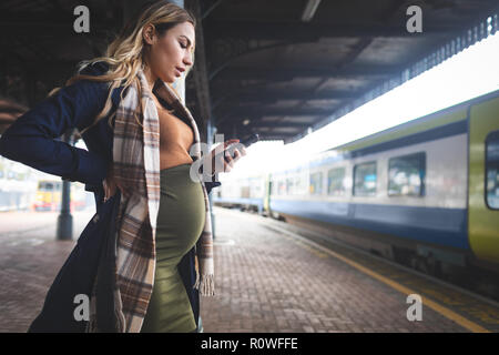 Pregnant woman using mobile phone at railway station Stock Photo