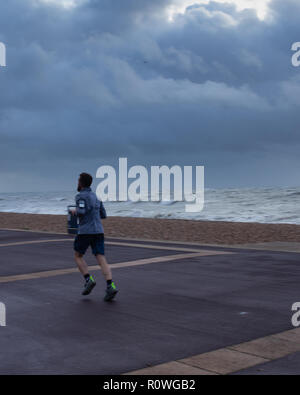 A man jobbing or running along the beach on a very stormy and windy day Stock Photo
