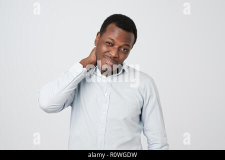 Confused african man scratching head while looking at camera and standing over gray background. Stock Photo