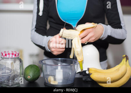 Woman in kitchen cuts banana with knife in blender. Fresh fruit for smoothie drink on desk. Detox and healthy food concept. Close up, selective focus Stock Photo