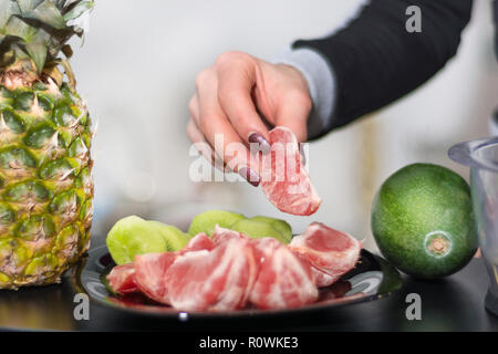 Woman hand holds red peeled grapefruit on plate. Healthy fruit salad on desk in kitchen. Close up, selective focus Stock Photo