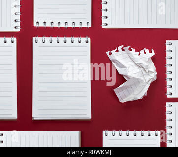 abstract red background with many notebooks with blank sheets in line and one crumpled sheet Stock Photo
