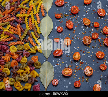 unprepared multi-colored pasta spiral made from wheat flour and cut into halves of cherry tomatoes with salt and spice Stock Photo