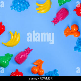 multicolored plastic toys fruits on a blue background, copy space Stock Photo