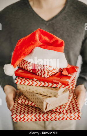 Young man holding and showing stack of gifts after wrapping. Lifestyle background. Stock Photo