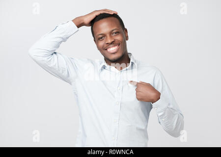 Portrait of proud handsome african man standing, looking at camera and pointing himself. Stock Photo